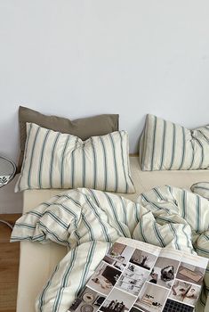 an unmade bed with striped sheets and pillows on it, next to a lamp