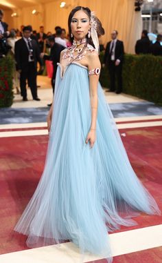 a woman in a blue gown standing on a red carpet with other people behind her