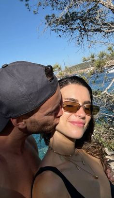 a man and woman kissing each other in front of the ocean on a sunny day