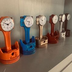 there are five different clocks on the wall together in this row, one is orange and one is blue