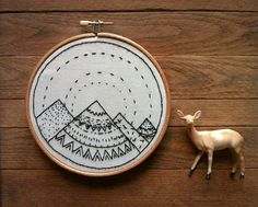 a deer is standing next to an embroidery hoop with mountains in the background and a mountain range on it