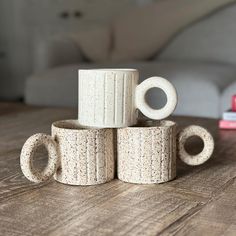 four white ceramic mugs stacked on top of each other in front of a couch