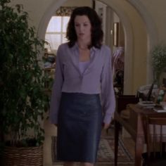 a woman standing in a living room next to a potted plant