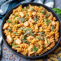 pasta with chicken and spinach in a black bowl on a blue tablecloth next to silverware