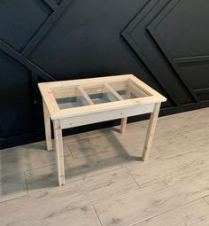 a small wooden table sitting on top of a hard wood floor next to a black wall