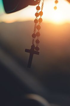 a person holding a rosary with the sun setting in the background