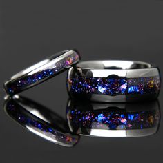 two wedding rings with blue and purple glitters on the inside are shown against a black background