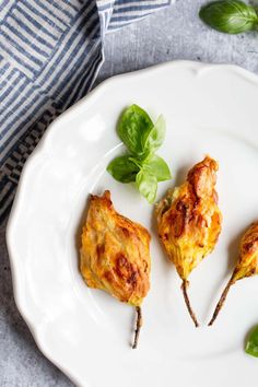 three chicken skewers on a white plate with basil sprigs next to them