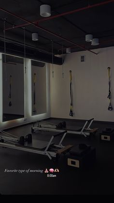 an empty gym room with equipment hanging from the ceiling and mirrors on the wall behind it