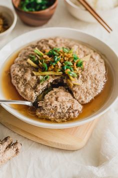 a white plate topped with meat covered in gravy next to chopsticks