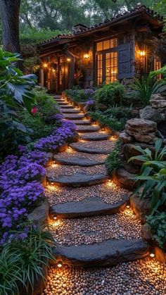 a stone path leading to a house surrounded by trees and flowers with lights on it