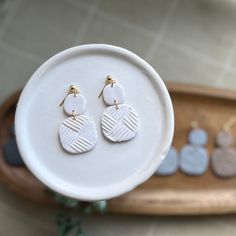 a pair of white and gold earrings sitting on top of a plate next to a wooden tray