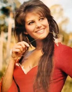 a woman with long hair smiling and holding a string in her mouth while wearing a red shirt