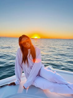 a woman sitting on the back of a boat at sunset