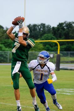 a football player jumping up in the air to catch a ball while another player tries to block it