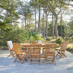 a wooden table and chairs sitting on top of a stone floor in front of trees