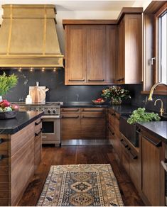 a kitchen with wooden cabinets and black counter tops, an area rug on the floor