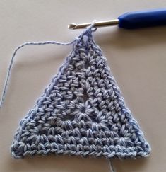 a crocheted triangle is shown with a knitting needle in the foreground and an object to the right of it