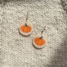 two orange pumpkins are hanging from small hoop earrings on a white knitted surface