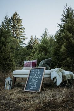 a chalkboard sign sitting on top of a grass covered field next to a forest