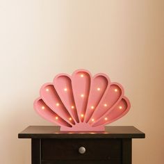 a pink shell shaped light sitting on top of a wooden table next to a white wall