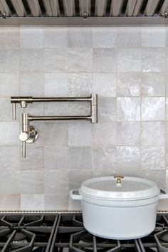 a white pot sitting on top of a stove next to a wall mounted faucet