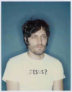 a man wearing a t - shirt with the word jesus written on it, in front of a blue background