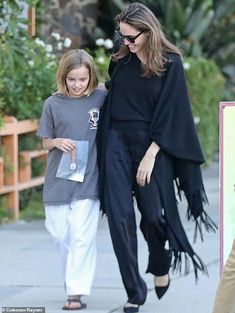 the mother and daughter are walking down the street together, both wearing black outfits with fringes