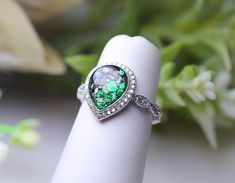 a close up of a ring on a finger with green and white stones in the middle