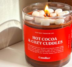 a candle with marshmallows in it sitting on a counter next to a bottle of hot cocoa and cozy cuddles