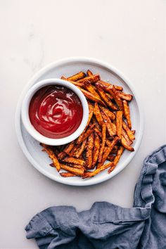 french fries on a plate with ketchup in a white bowl next to it