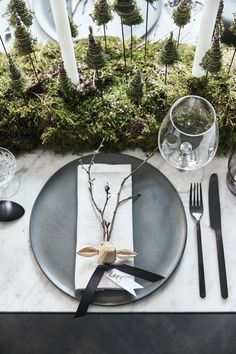 a place setting with moss and silverware on a marble table cloth, surrounded by candles