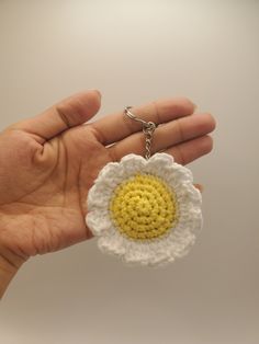 a hand holding a crocheted keychain with a yellow and white flower on it