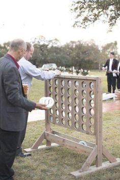 two men in suits are playing an outdoor game with beer cups on the sidelines