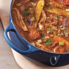 a blue pot filled with stew on top of a wooden table next to a cutting board