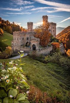 an old castle on top of a hill surrounded by trees and flowers in the foreground