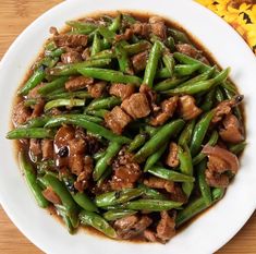 a white plate topped with green beans covered in meat and sauce on top of a wooden table