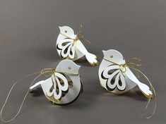 three white paper birds with gold string tied around them on a gray surface, one is shaped like a bird and the other has an ornament attached to it's wings