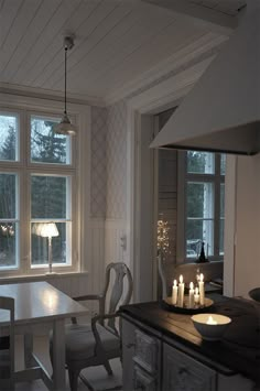 a dining room table with candles on it in front of two windows and a stove