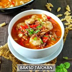 two bowls filled with soup on top of a wooden table next to pasta and basil leaves