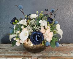 a vase filled with blue and white flowers sitting on top of a wooden table next to a gray wall