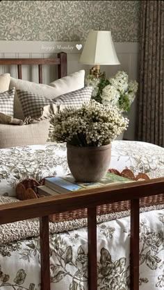 a flower pot on top of a bed in a room with floral wallpaper and pillows