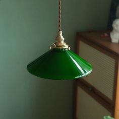 a green light hanging from a ceiling in a room with a dresser and cabinet behind it