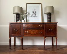 two lamps are sitting on top of a wooden dresser next to a painting and lamp shades