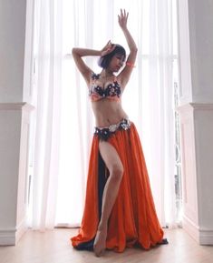 a woman in an orange and black belly dance outfit is posing for the camera with her hands behind her head