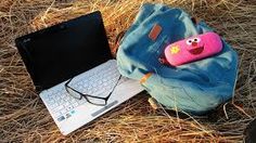 an open laptop computer sitting on top of a blue bag next to a pink stuffed animal