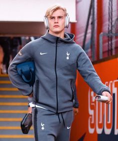 a man with headphones on walking down the runway in grey tracksuits and holding his hands behind his back