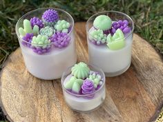 three desserts with purple and green decorations in small glass dishes on a wood slice