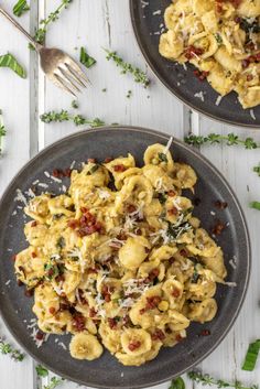 two plates filled with pasta and cheese on top of a white wooden table next to silverware