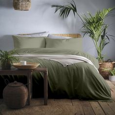 a bed with green sheets and pillows in a room next to a potted plant